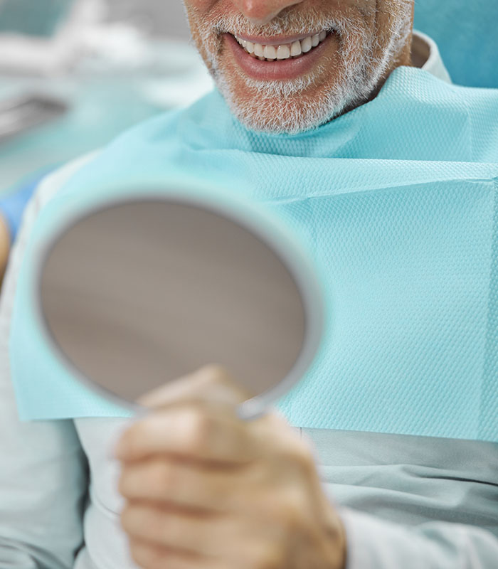 Elderly man holding a mirror and smiling while sitting in a dental office
